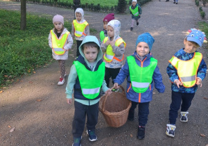 2. Przedszkolaki z koszem wiklinowym idą alejką parku.