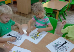 13. Dziewczynki siedzą przy stoliku i ozdabiają sylwety drzew.