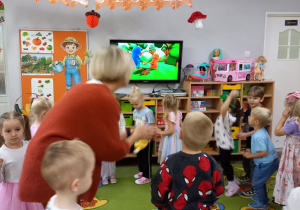 2. Dzieci z nauczycielką wykonują zabawę ruchowa do piosenki Let s play z tyłu ekran telewizora, na którym przedstawiony jest przebieg zabawy.
