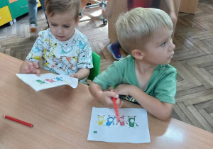6. Chłopcy siedzą przy stolikach na krzesłach i kolorują żuczki.