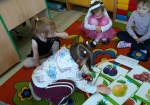 12. Dziewczynka wybiera obrazek spośród owoców leżących na dywanie.