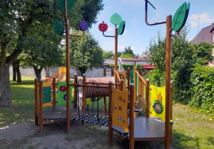 Urządzenie terenowe ze zjeżdżalnią, mostkiem linowym i tunelem. W tle drzewa.