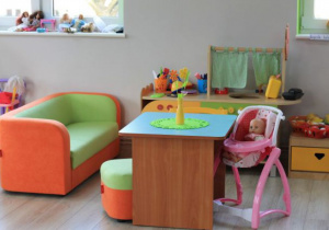 Kącik domowy w grupie III "Biedronki" - obok stolika stoi kanapa, pufa, stojak z lalką, a za nim kuchnia dla dzieci.